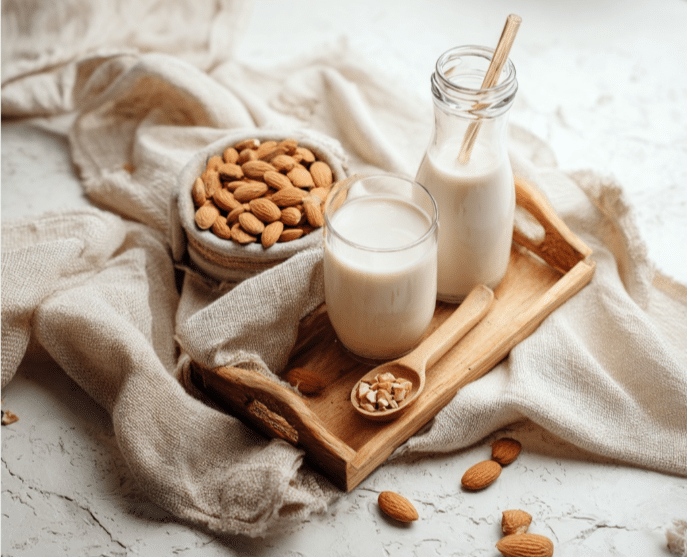 Almond milk creamer with minimal almonds on a wooden tray, styled on marble with soft beige linen.